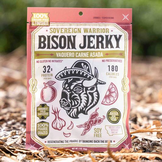 A package of Jockoo Sovereign Warrior Bison Jerky stands upright on a bed of mulch outdoors, with a blurred green garden background.